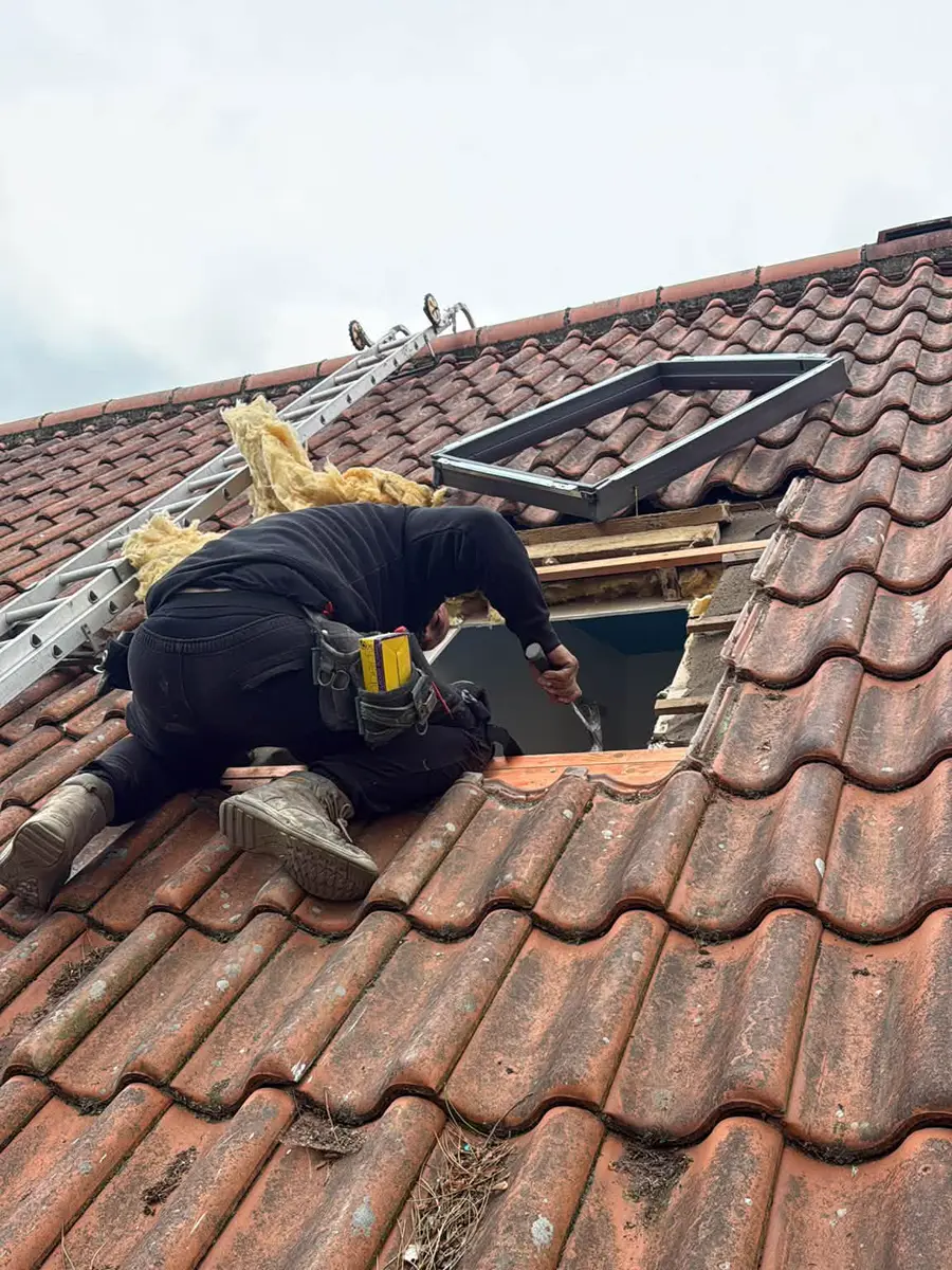 One of the Fox Roofing team kneeling on a clay tiled roof, fitting a roof window