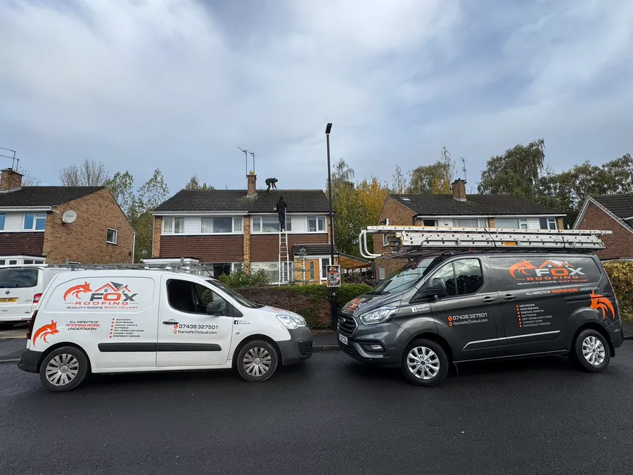 Both Fox Roofing vans parked outside a job, with one of the team on the roof and another on the ladder