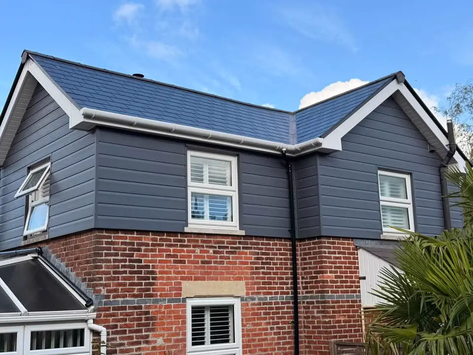White fascias and black guttering along a grey tiled roof, with grey cladding below