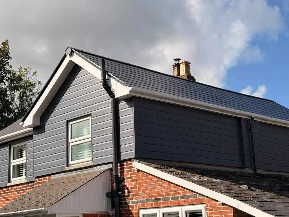 A gable with a white fascia and bargeboard over grey cladding, with a black gutter and downpipe