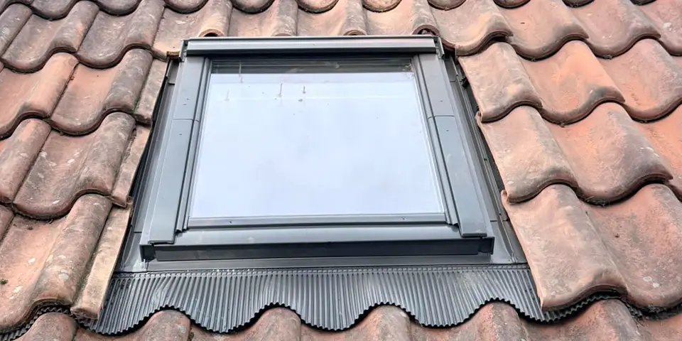 A roof window fitted into a clay pantile roof, its flashing dressed over the tiles