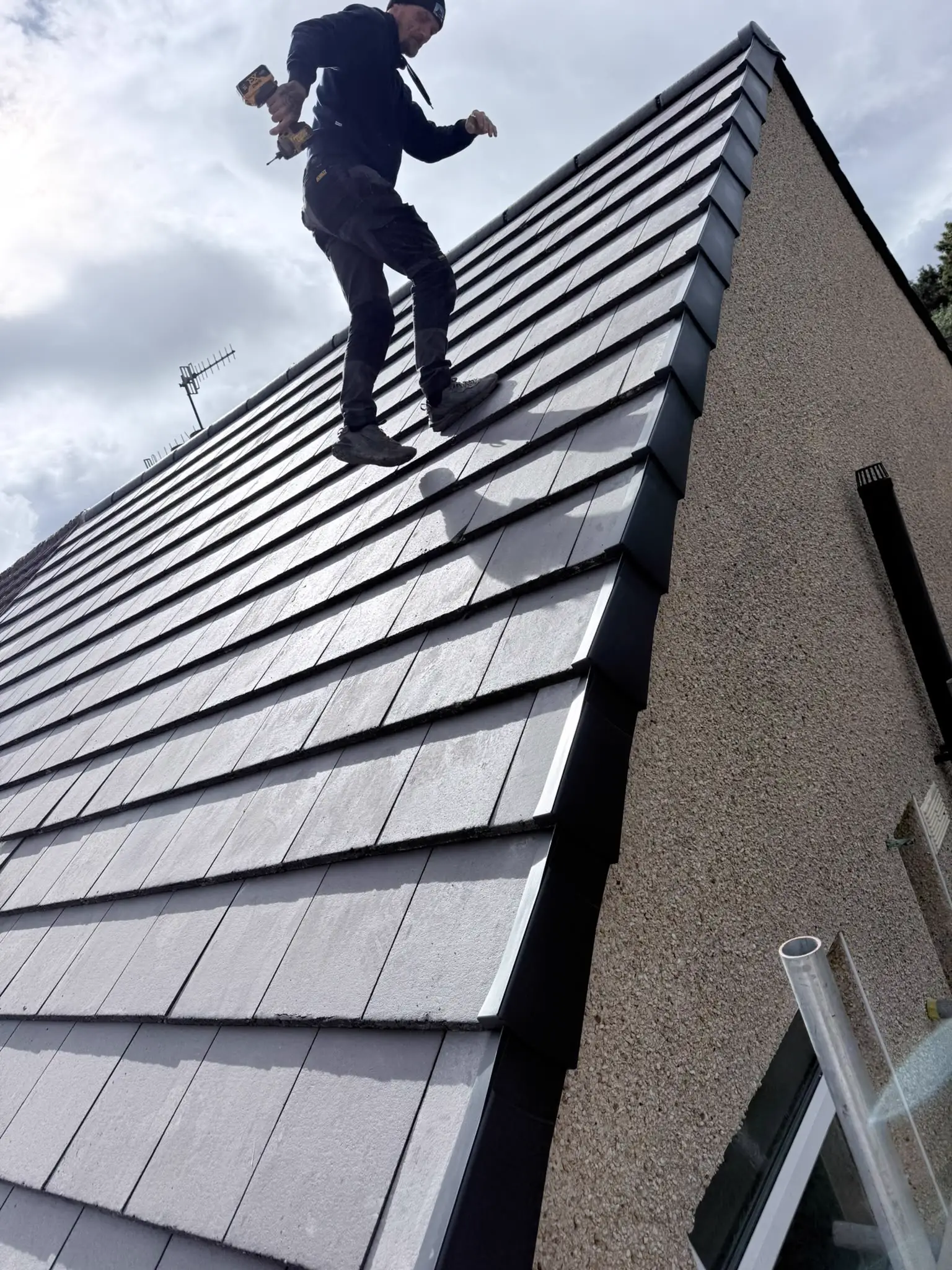 A roofer fixing new grey tiles on a pitched roof, with a dry verge along the gable