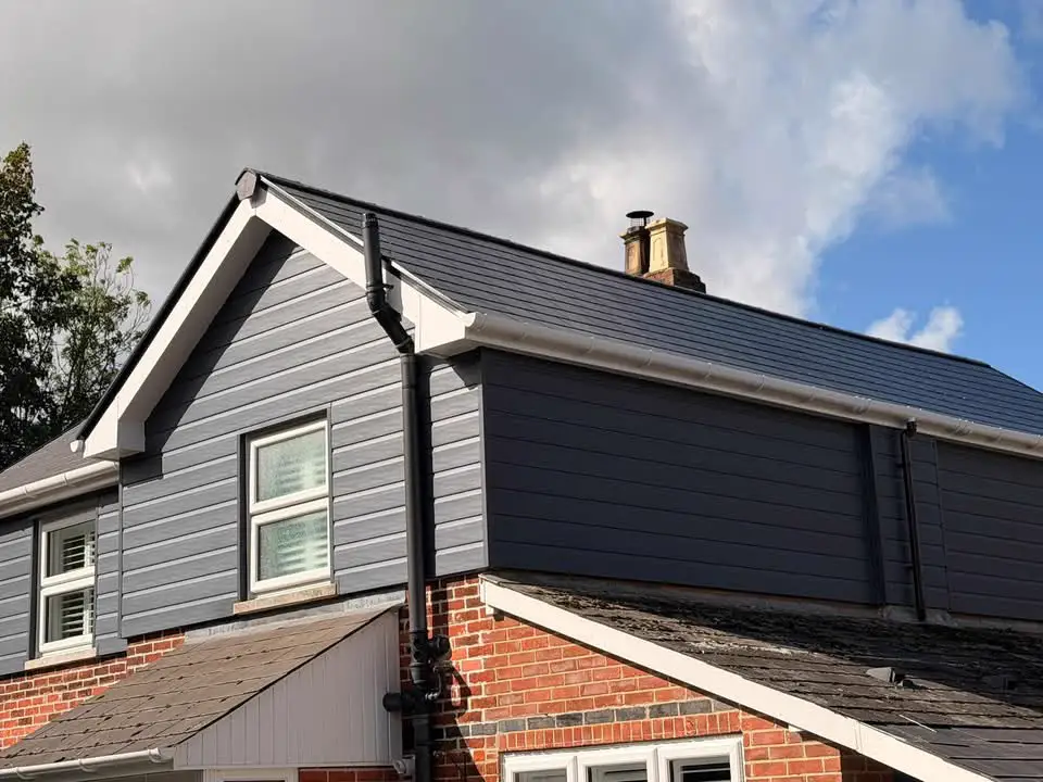 A gable with a white fascia and bargeboard over grey cladding, with a black gutter and downpipe