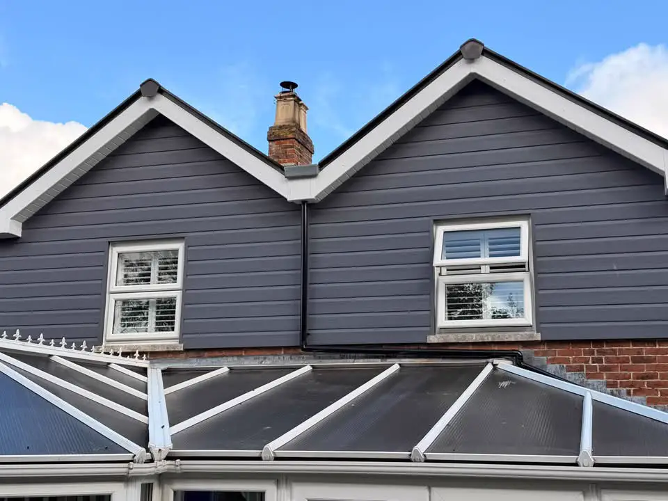 Twin gables with white bargeboards and fascias over grey cladding, above a conservatory