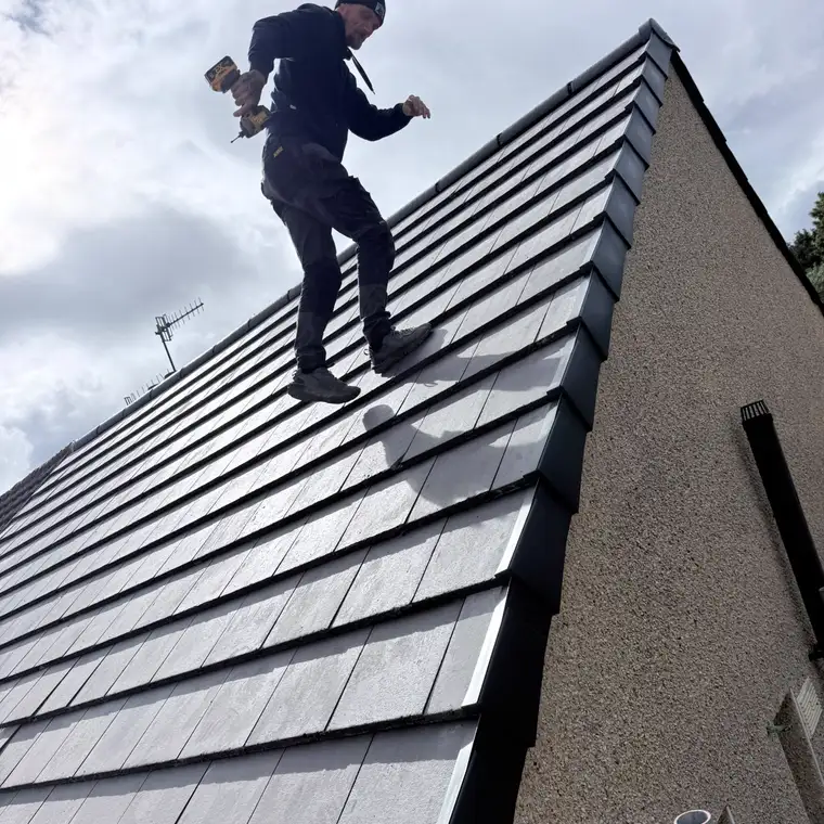 A roofer fixing a newly laid grey tiled roof with a dry verge along the gable