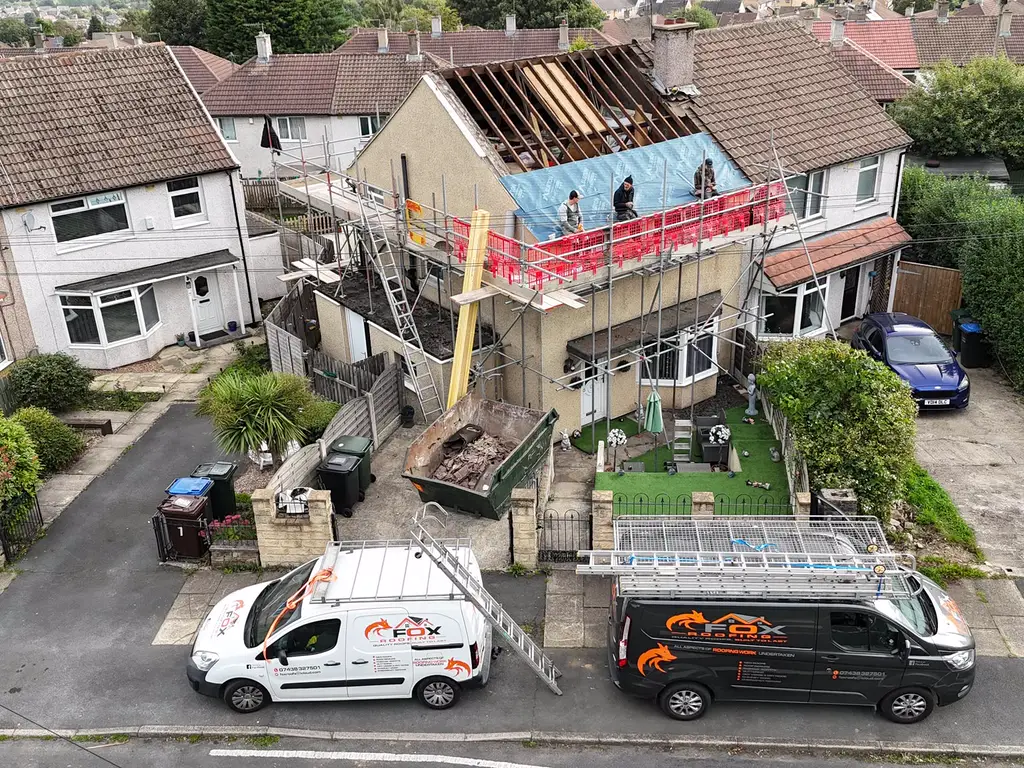 From above: the team on the scaffold of a re-roof, the old tiles stripped, with both Fox Roofing vans parked out front